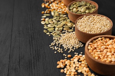 Photo of Different types of seeds and cereals in bowls on black wooden table, closeup. Space for text