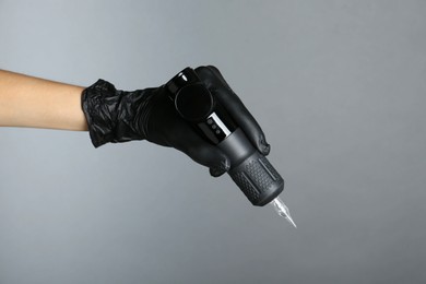 Photo of Professional cosmetologist holding permanent makeup machine on grey background, closeup