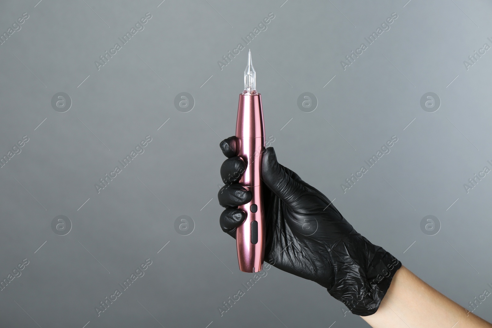 Photo of Professional cosmetologist holding permanent makeup machine on grey background, closeup. Space for text