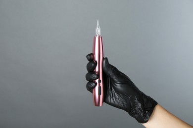 Photo of Professional cosmetologist holding permanent makeup machine on grey background, closeup. Space for text