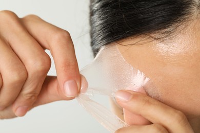 Woman peeling off face mask on light grey background, closeup