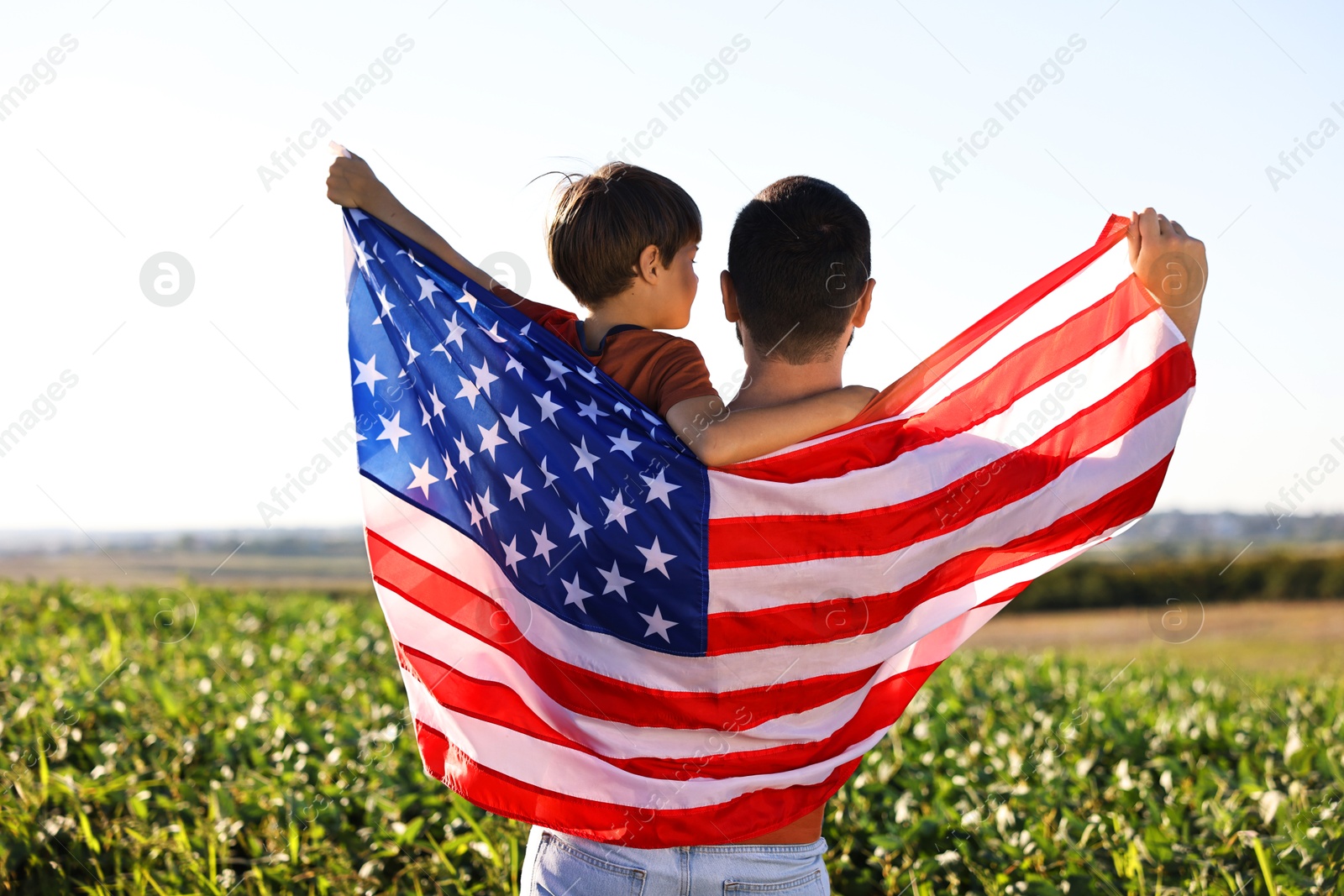 Photo of Father and son with flag of USA outdoors, back view