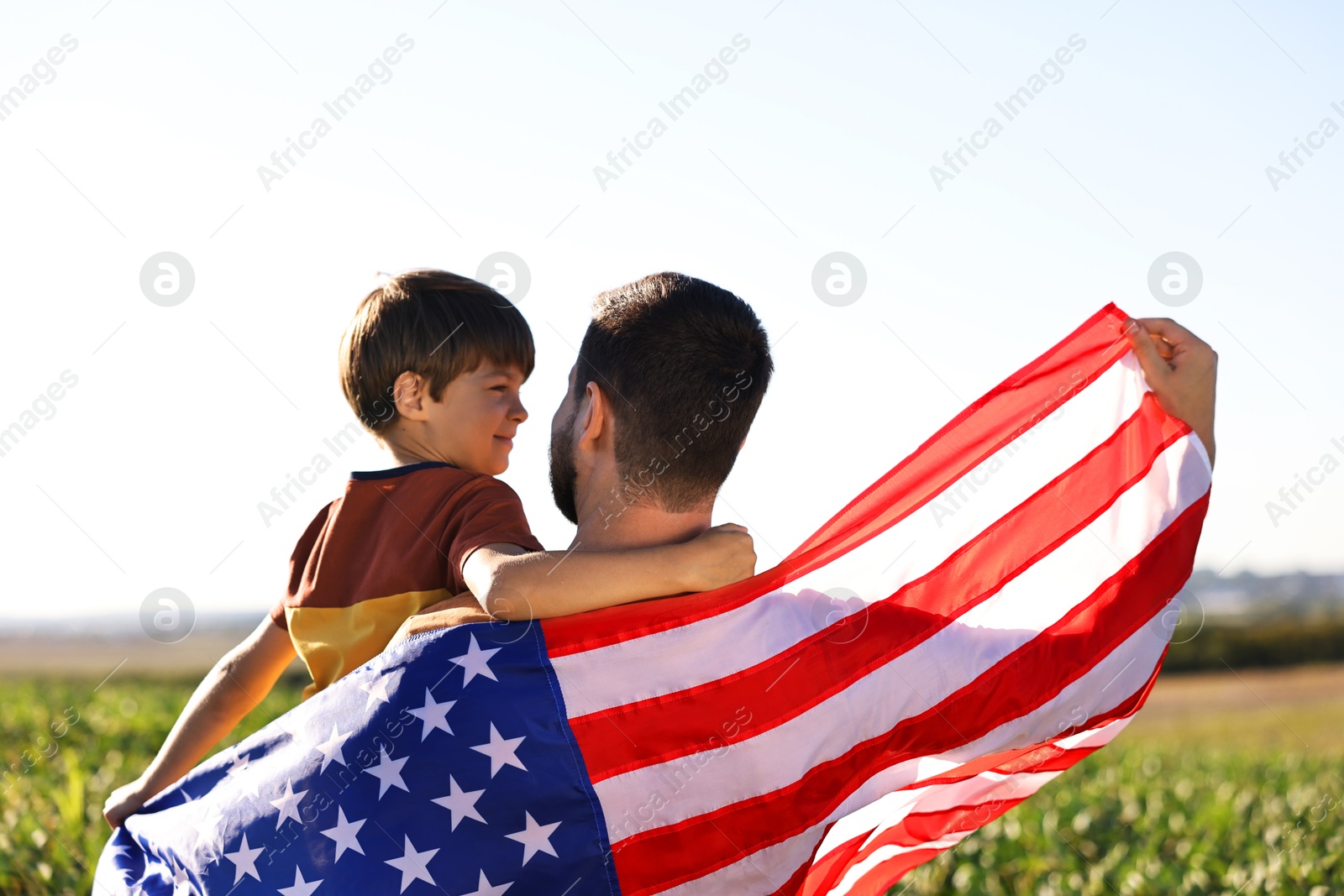 Photo of Father and son with flag of USA outdoors, back view