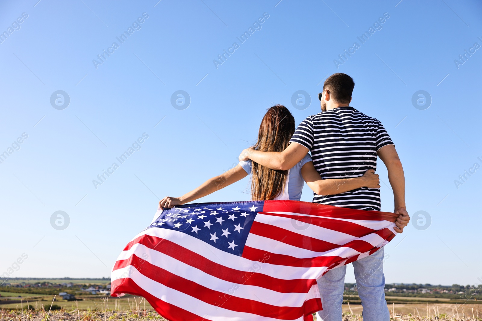 Photo of Couple with flag of USA outdoors, back view. Space for text