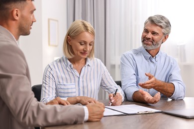 Pension plan. Couple consulting with insurance agent at table indoors