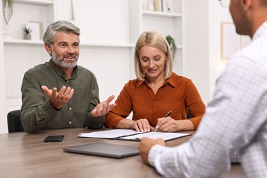 Photo of Pension plan. Couple consulting with insurance agent at table indoors