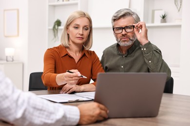 Pension plan. Couple consulting with insurance agent at table indoors