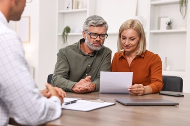 Pension plan. Couple consulting with insurance agent at table indoors