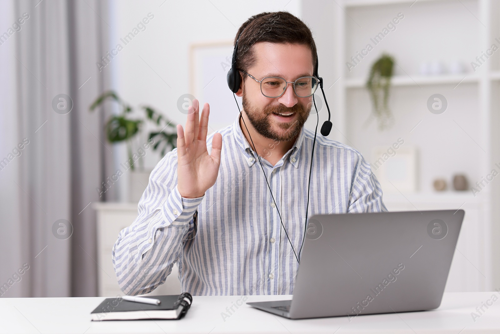 Photo of Interpreter in headset having video chat via laptop at white table indoors