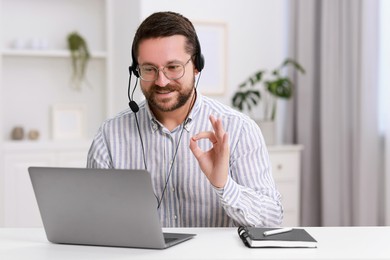 Interpreter in headset having video chat via laptop at white table indoors