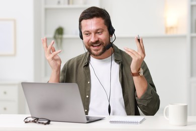 Interpreter in headset having video chat via laptop at white table indoors