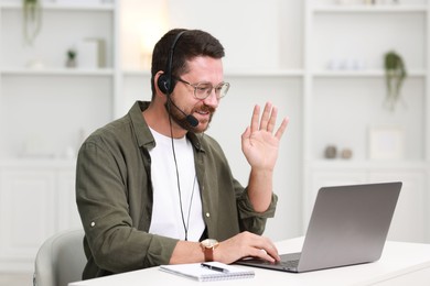 Interpreter in headset having video chat via laptop at white table indoors