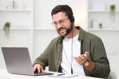 Interpreter in headset having video chat via laptop at white table indoors