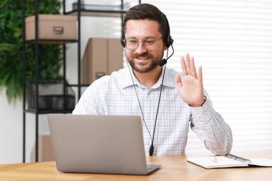 Interpreter in headset having video chat via laptop at wooden table indoors