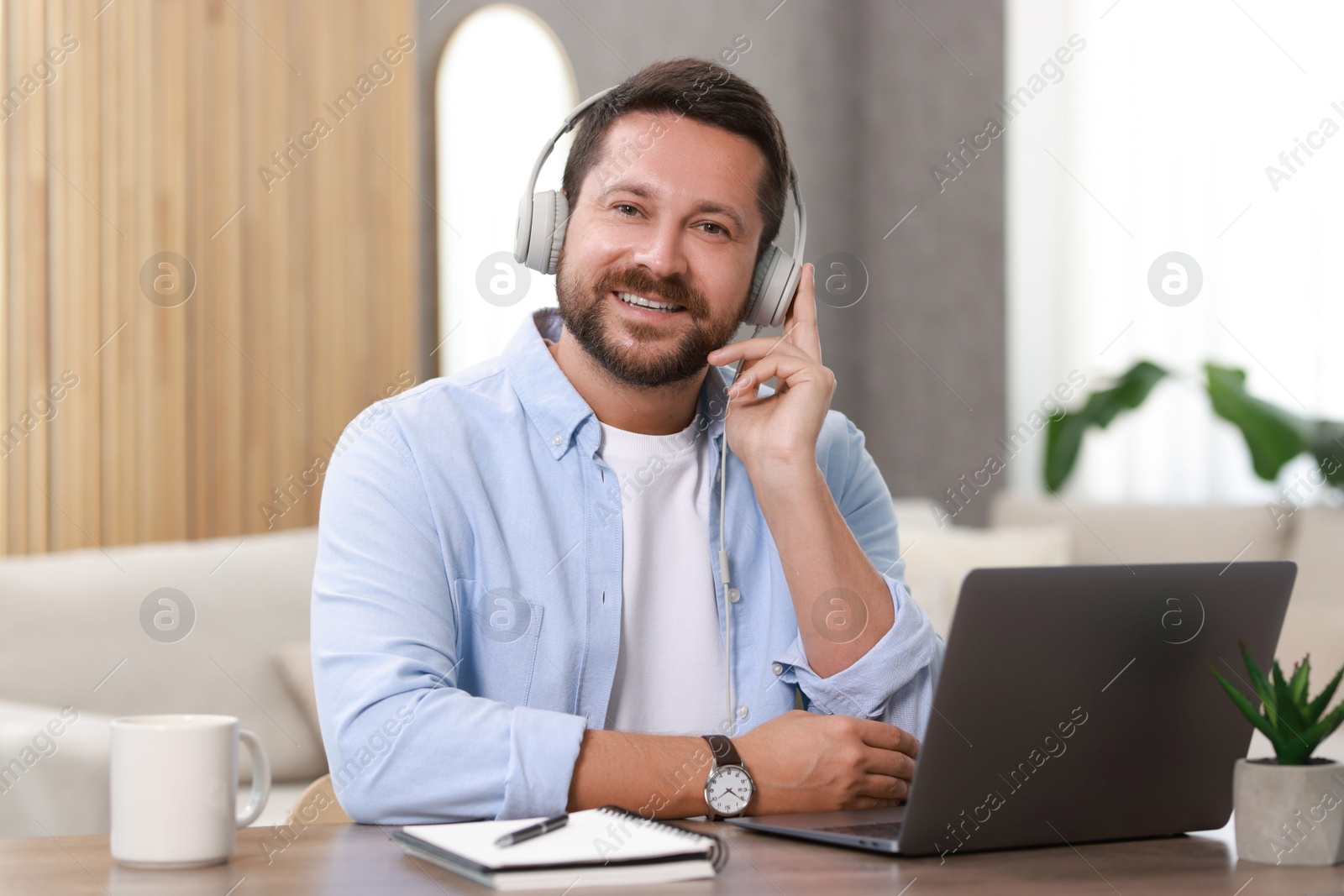 Photo of Interpreter in headphones having video chat via laptop at wooden table indoors