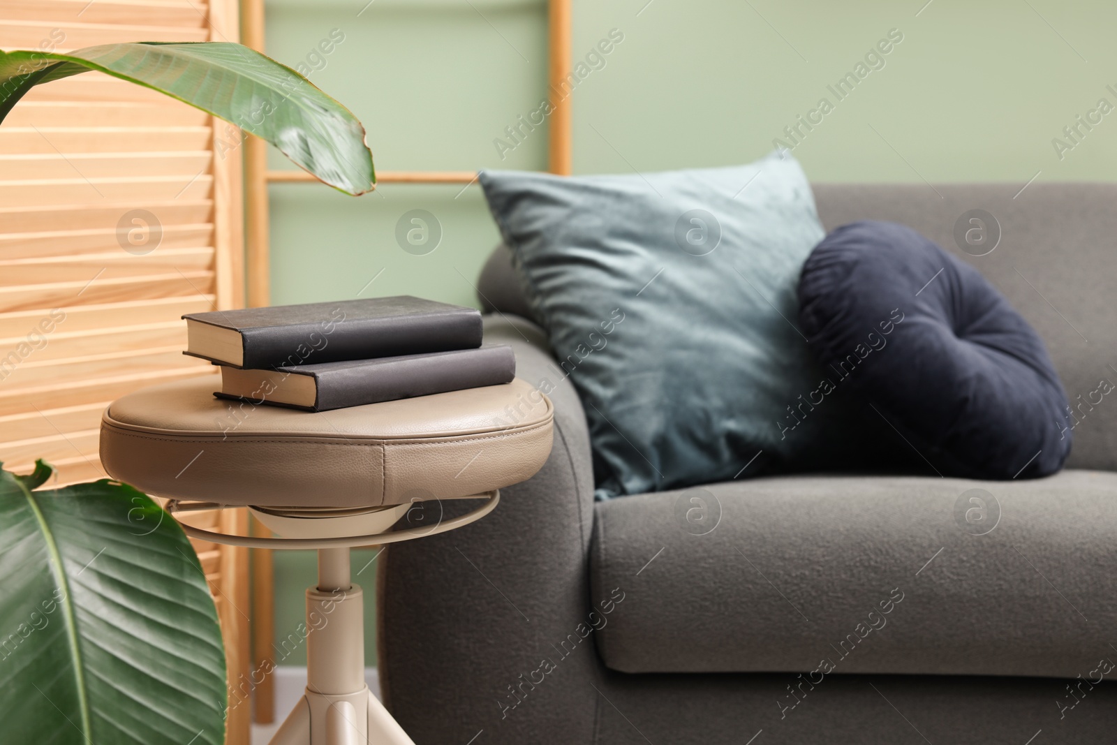 Photo of Stool with books and sofa in room. Stylish interior design