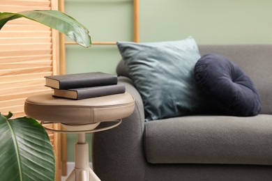 Photo of Stool with books and sofa in room. Stylish interior design