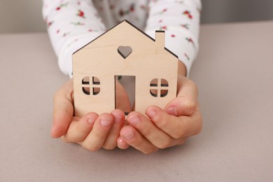 Photo of Adoption. Little girl with house figure at beige table, closeup