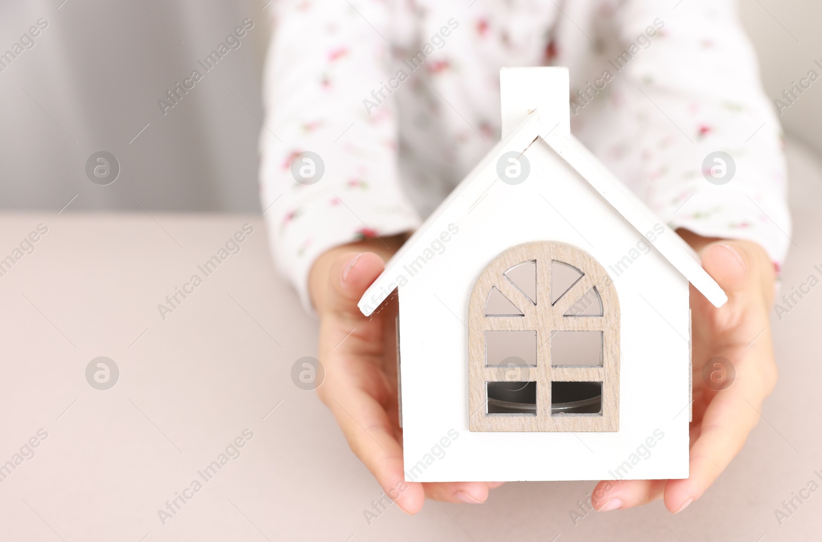 Photo of Adoption. Little girl with house figure at beige table, closeup. Space for text