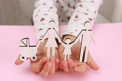 Photo of Adoption. Little girl with figures of family at pink table, closeup