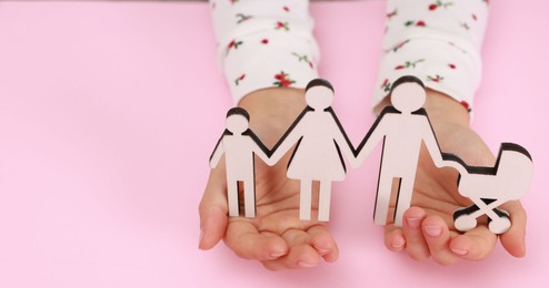 Photo of Adoption. Little girl with figures of family on pink background, closeup. Space for text