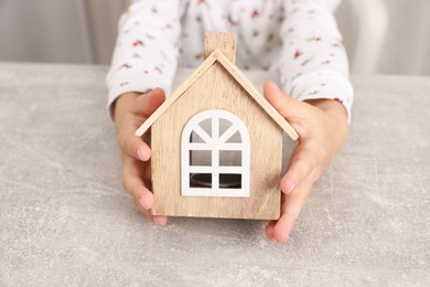 Photo of Adoption. Little girl with house figure at grey table, closeup