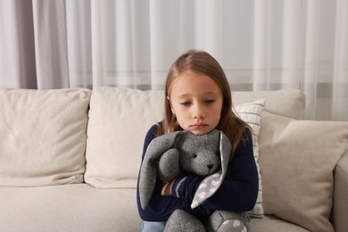 Autism concept. Lonely little girl with toy bunny on sofa at home