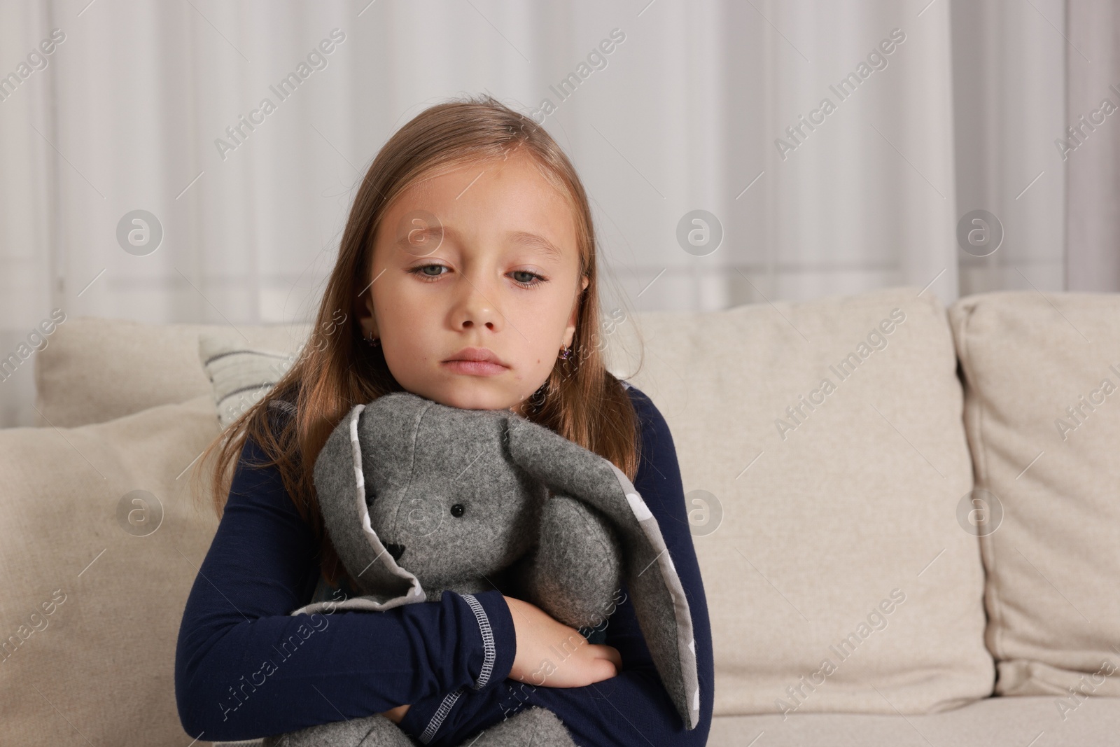 Photo of Autism concept. Lonely little girl with toy bunny on sofa at home