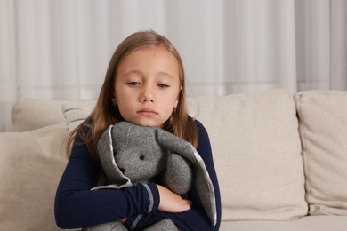 Autism concept. Lonely little girl with toy bunny on sofa at home