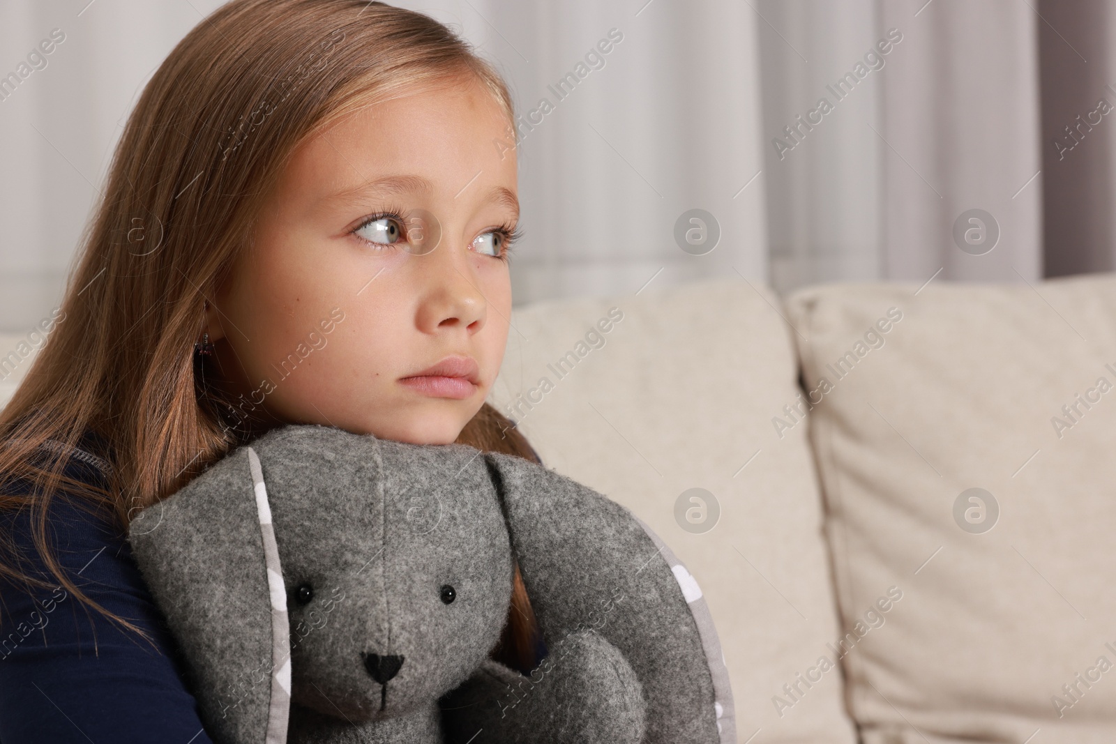 Photo of Autism concept. Lonely little girl with toy bunny on sofa at home, space for text