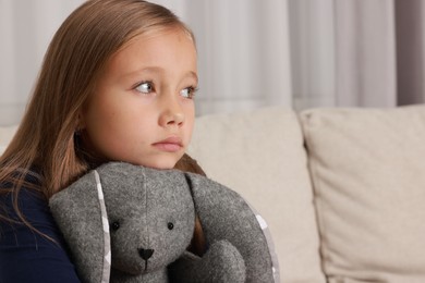 Autism concept. Lonely little girl with toy bunny on sofa at home, space for text