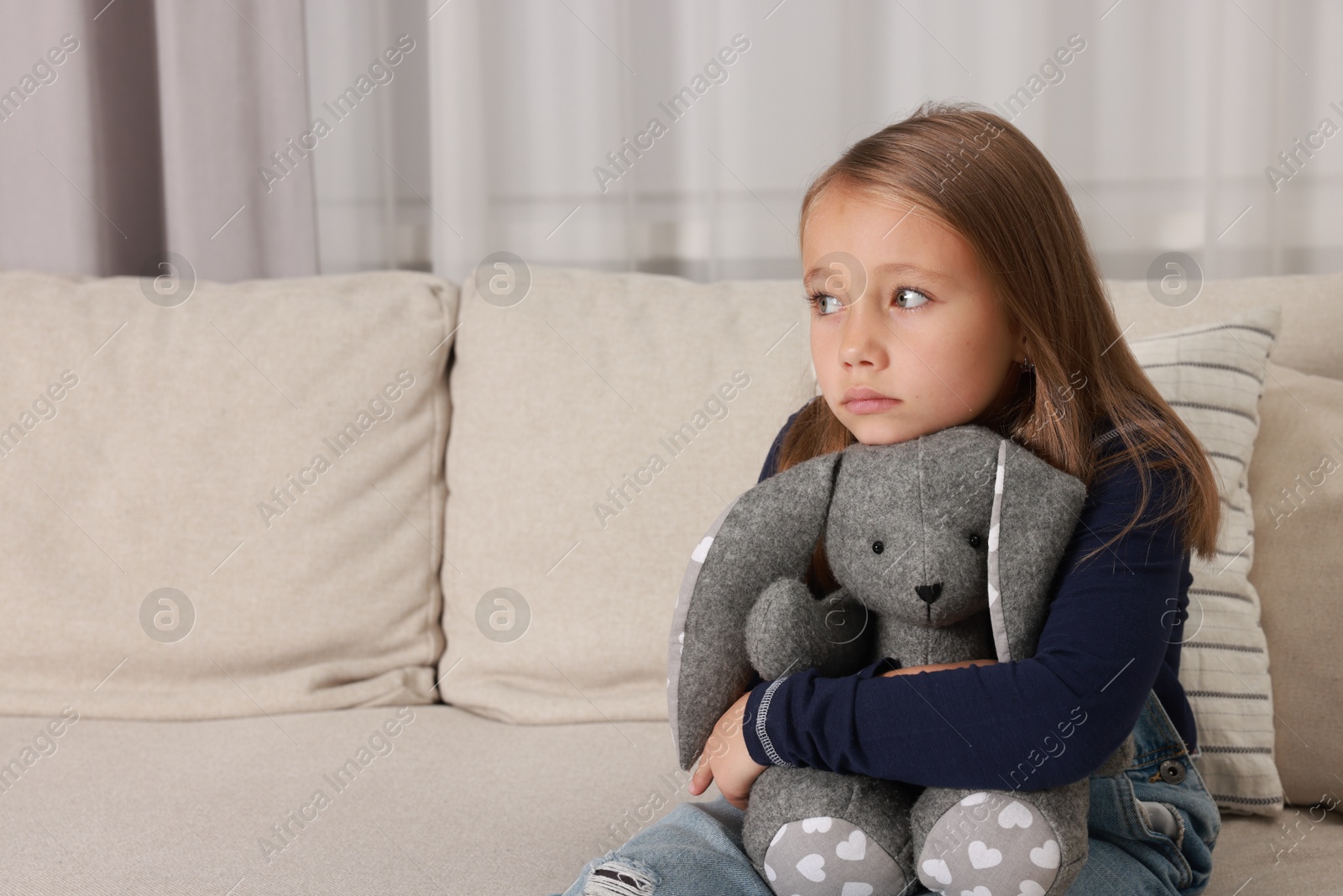 Photo of Autism concept. Lonely little girl with toy bunny on sofa at home