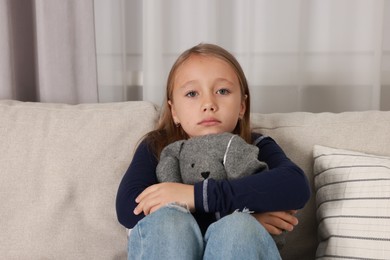 Autism concept. Lonely little girl with toy bunny on sofa at home