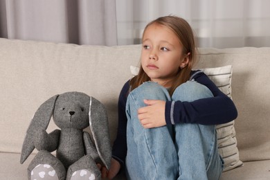 Autism concept. Lonely little girl with toy bunny on sofa at home