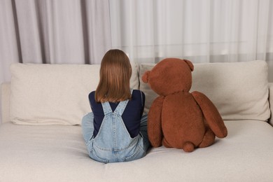 Photo of Autism concept. Lonely little girl with teddy bear on sofa at home, back view