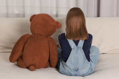 Autism concept. Lonely little girl with teddy bear on sofa at home, back view