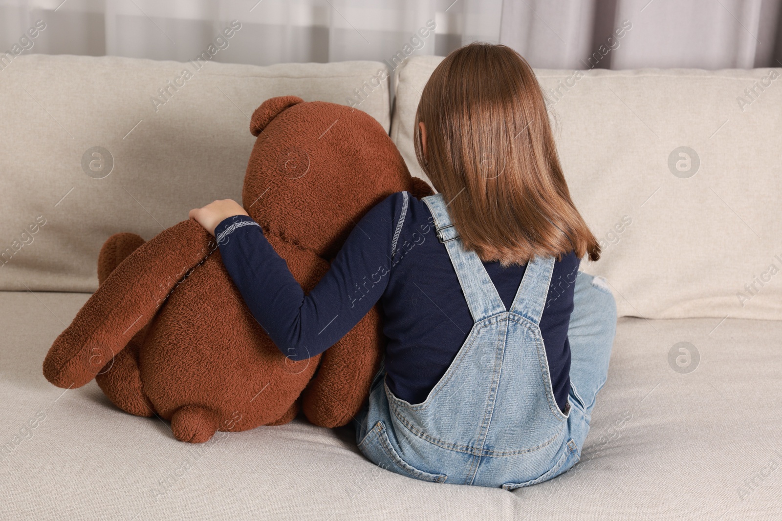 Photo of Autism concept. Lonely little girl with teddy bear on sofa at home, back view