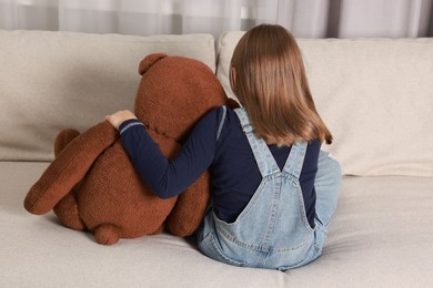 Autism concept. Lonely little girl with teddy bear on sofa at home, back view