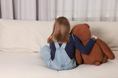 Photo of Autism concept. Lonely little girl with teddy bear on sofa at home, back view