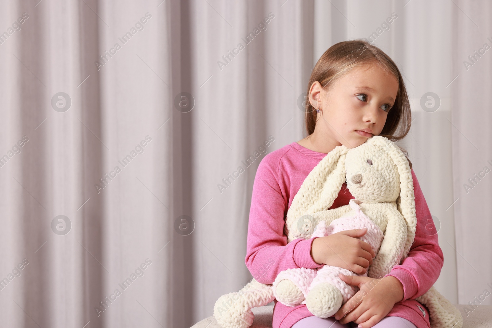 Photo of Autism concept. Lonely little girl with toy bunny on pouf at home, space for text