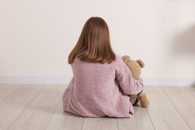 Autism concept. Lonely little girl with teddy bear on floor at home, back view