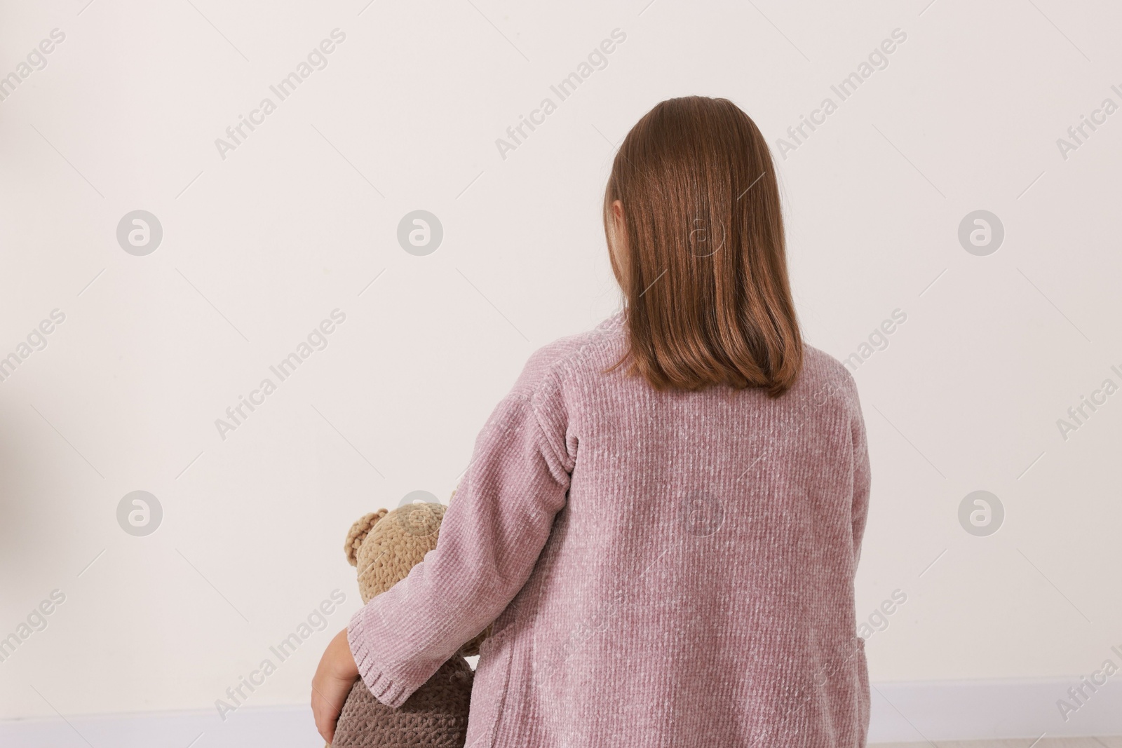 Photo of Autism concept. Lonely little girl with teddy bear against beige wall at home, back view