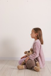 Autism concept. Lonely little girl with teddy bear on floor at home