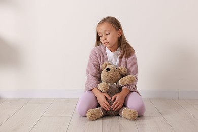 Autism concept. Lonely little girl with teddy bear on floor at home