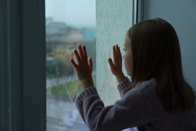 Autism concept. Lonely little girl near window at home