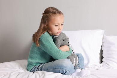 Autism concept. Lonely little girl with toy bunny on bed at home