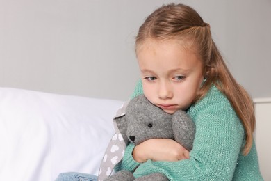 Photo of Autism concept. Lonely little girl with toy bunny on bed at home, space for text