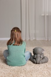 Autism concept. Lonely little girl with toy bunny on floor at home, back view