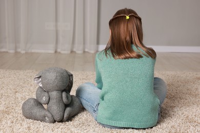 Photo of Autism concept. Lonely little girl with toy bunny on floor at home, back view