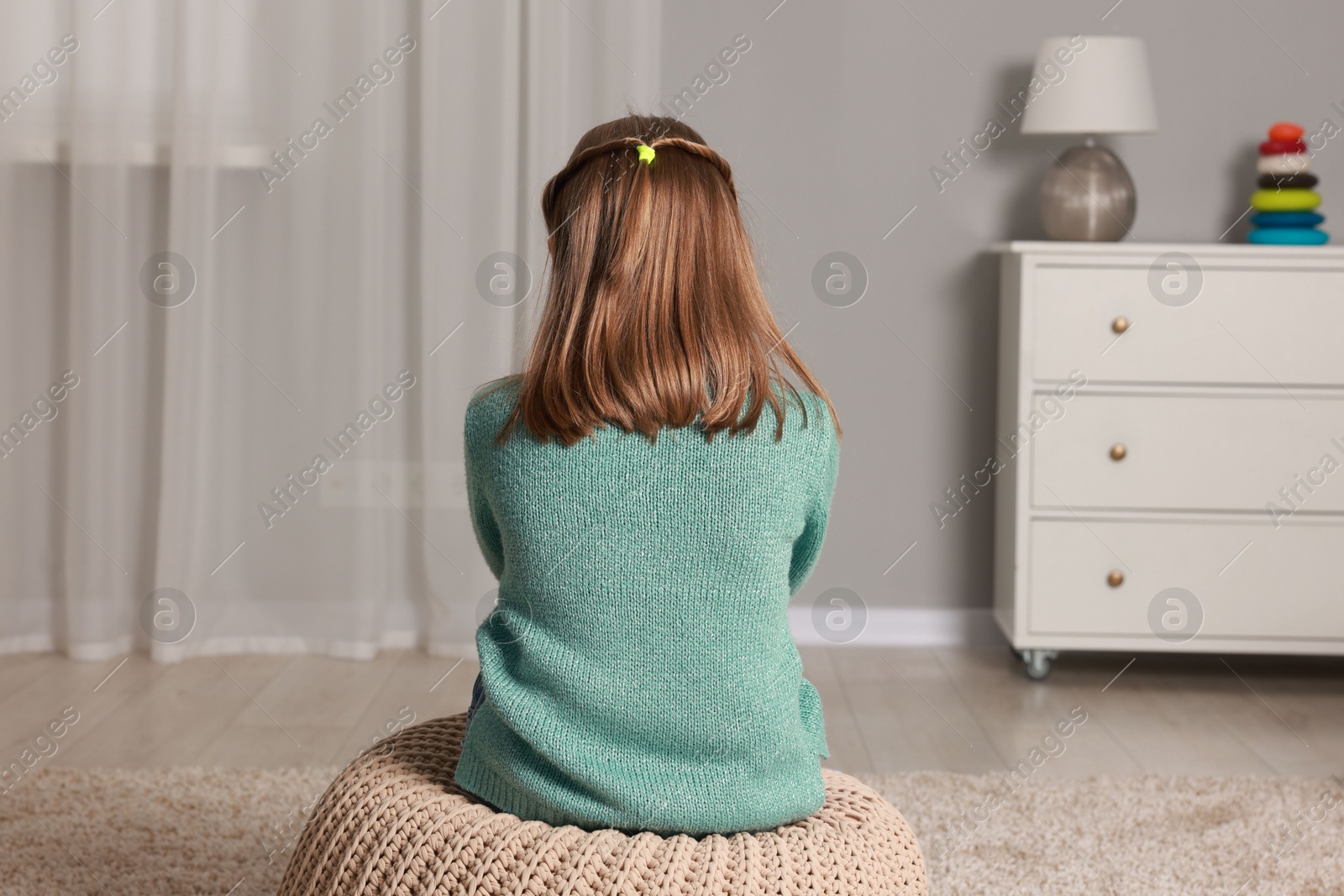 Photo of Autism concept. Lonely little girl on pouf at home, back view